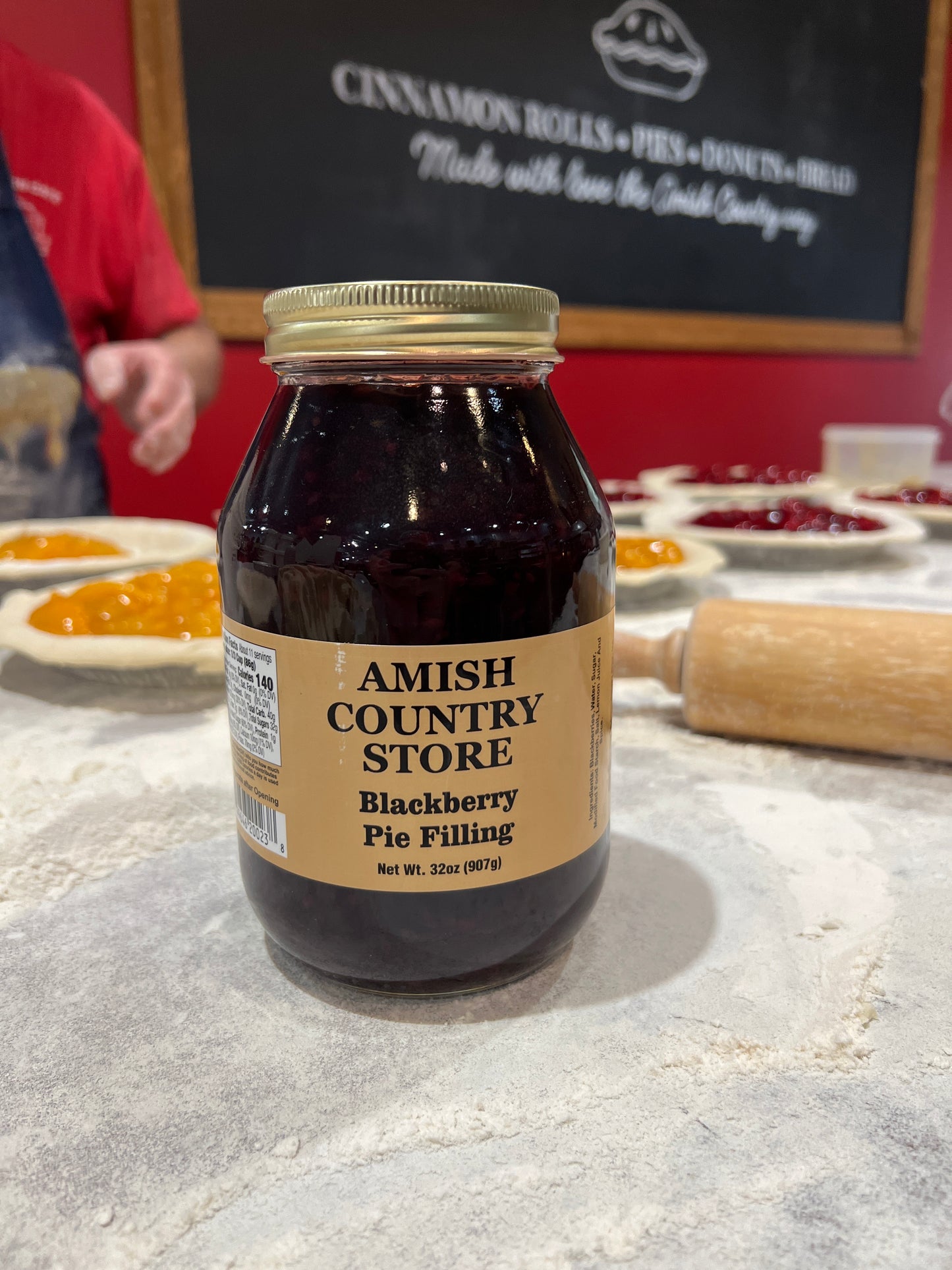 Amish Country Store blackberry pie filling jar on a concrete surface with a chalkboard in the background.