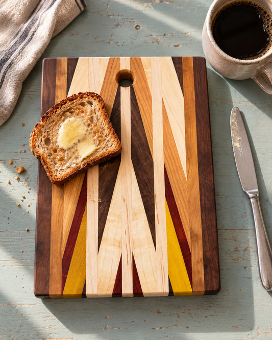 Amish-made chevron cutting and serving board with one slice of toast in a styled breakfast scene; one board per purchase, food and props not included.