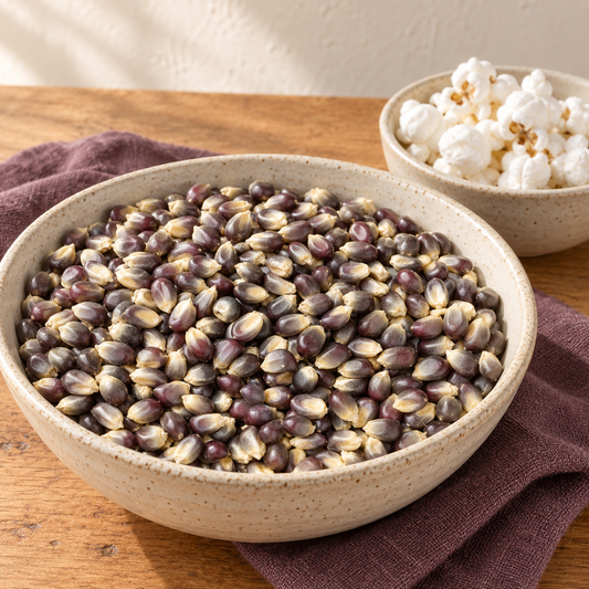 Blue popcorn kernels in a cream bowl with a smaller bowl of popped corn on a wooden table