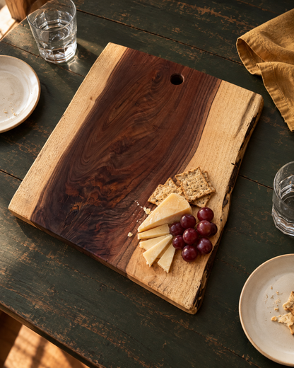 Wider live-edge board with a small serving of cheese, crackers and grapes on a green table; an example of natural grain and footprint variation.