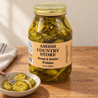 32 fl oz Amish Country Store Bread & Butter Pickles jar beside crinkle-cut pickle slices and pickled onion in a dish.
