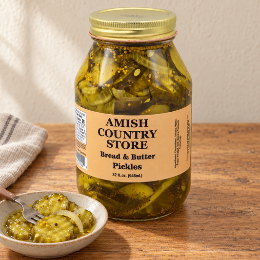 32 fl oz Amish Country Store Bread & Butter Pickles jar beside crinkle-cut pickle slices and pickled onion in a dish.