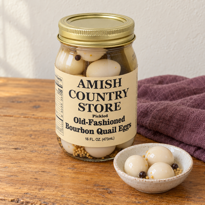 Pickled Old-Fashioned Bourbon Quail Eggs (16 oz) in its original labeled jar with a small serving beside it on a warm wood table.