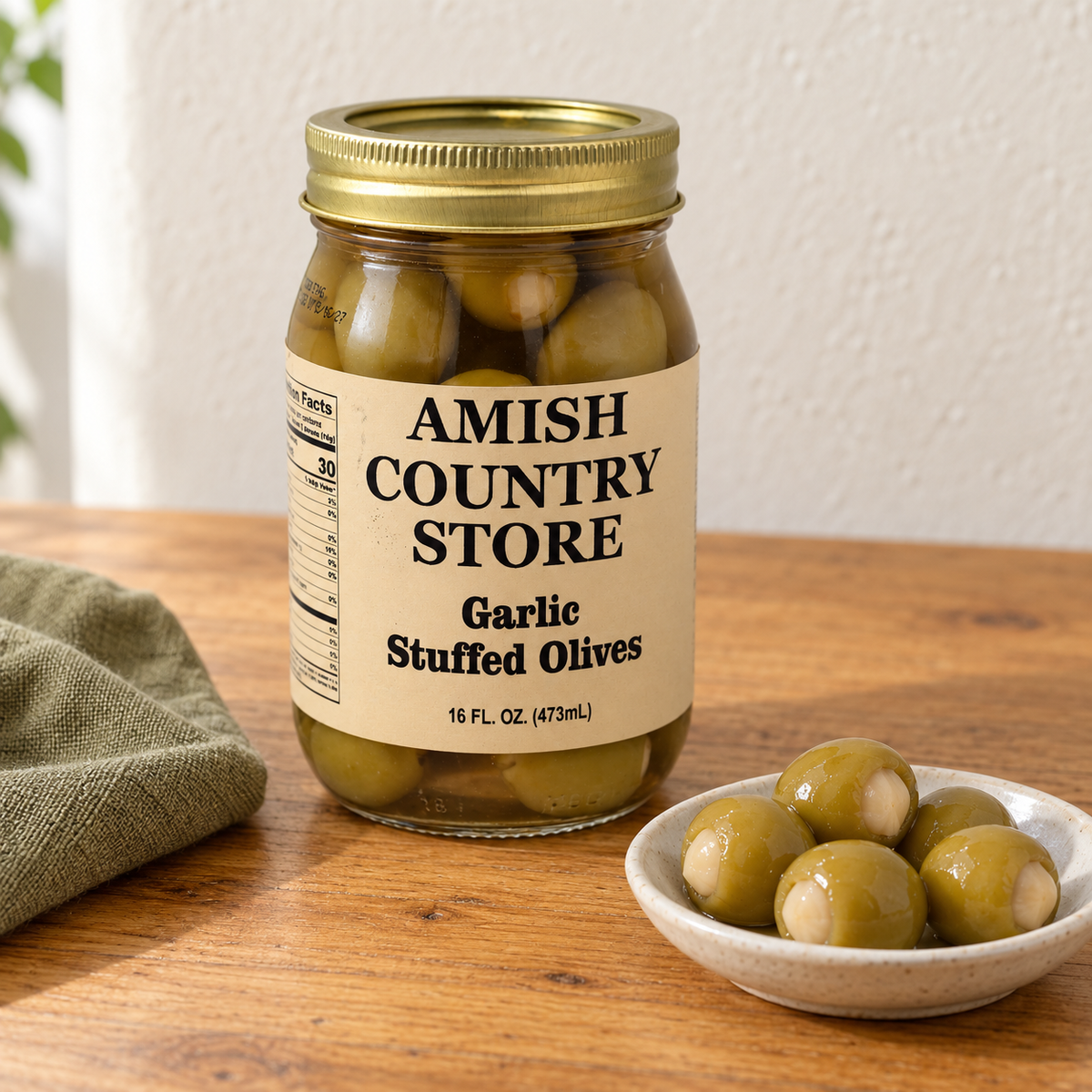 Amish Country Store Garlic Stuffed Olives, 16 fl oz jar, beside a small serving of olives with garlic filling.