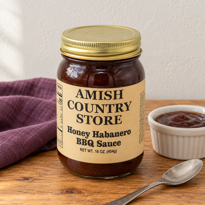 Amish Country Store Honey Habanero BBQ Sauce,16oz jar beside a small dish of dark barbecue sauce.