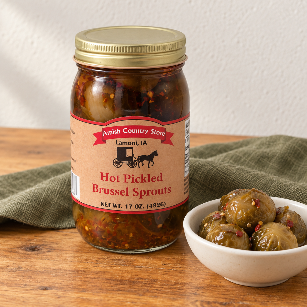 Hot Pickled Brussels Sprouts in its original labeled jar with a small serving beside it on a warm wood table.