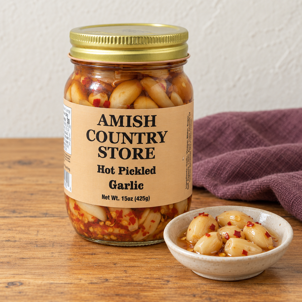 Amish Country Store Hot Pickled Garlic,15oz jar beside garlic cloves in chili-flecked brine.