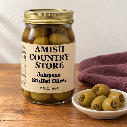 Amish Country Store Jalapeno Stuffed Olives, 16 fl oz jar, beside a small serving of green olives with jalapeno filling.