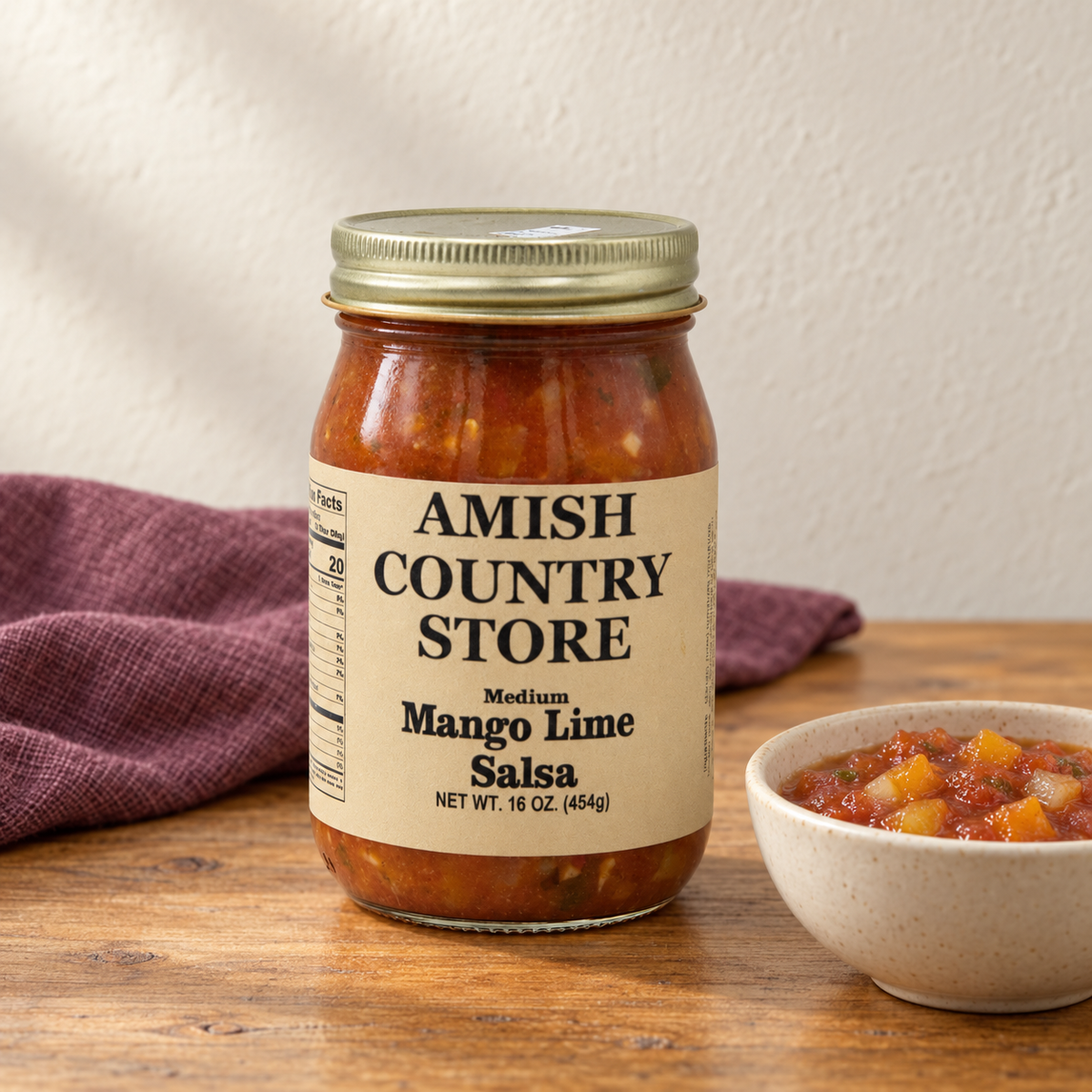 Medium Mango Lime Salsa in its original labeled jar with a small serving beside it on a warm wood table.