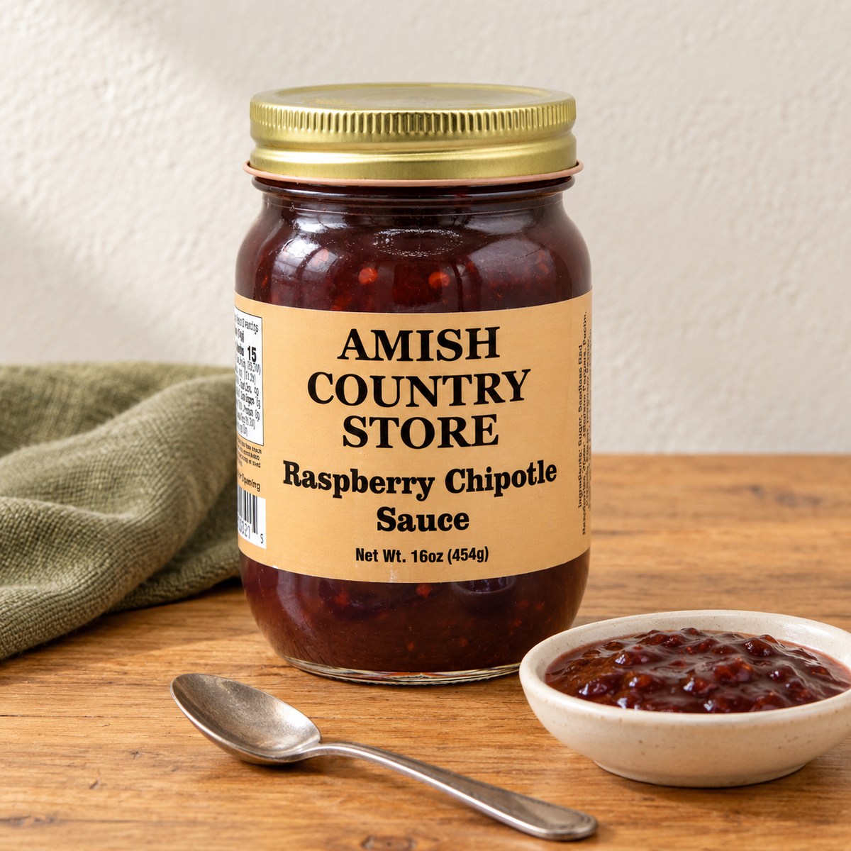 Amish Country Store Raspberry Chipotle Sauce,16oz jar beside a small serving of burgundy sauce.