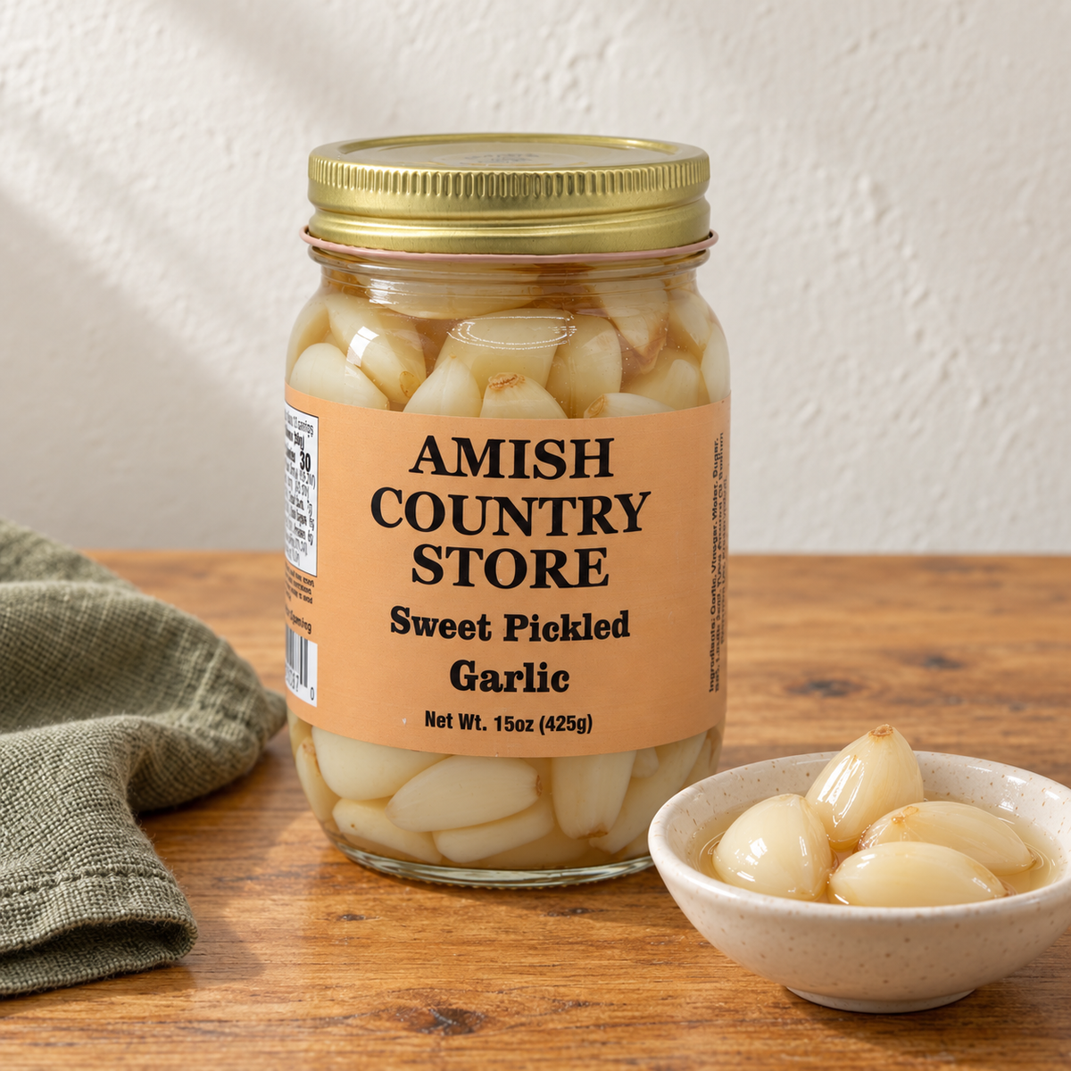 Sweet Pickled Garlic in its original labeled jar with a small serving beside it on a warm wood table.