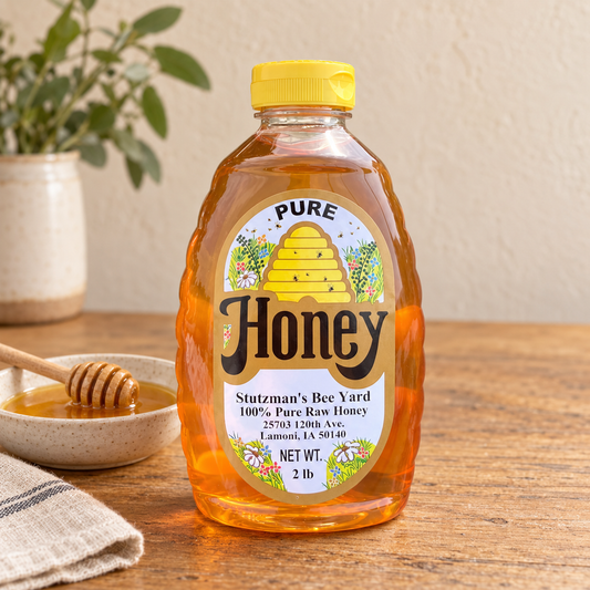 Stutzman’s Bee Yard Pure Honey 2 lb bottle beside a dish of honey and wooden dipper.