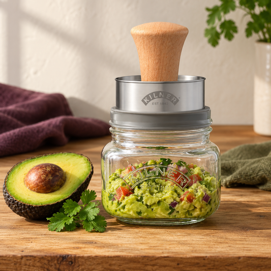 Kilner 500 mL Mash and Store Set assembled with its grey collar and wooden-handled masher, shown preparing guacamole.