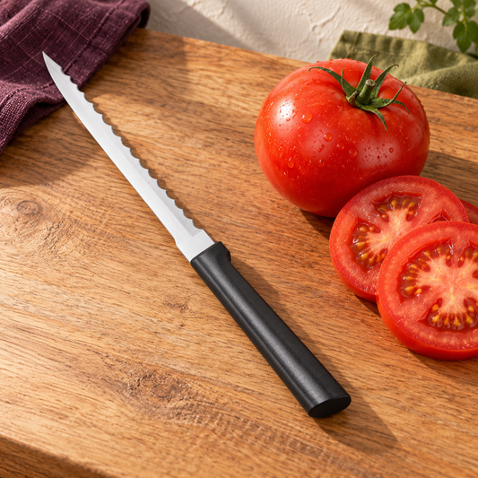 Black-handled Rada Tomato Slicer beside a tomato and slices on warm wood in an ivory, plum and olive kitchen scene.