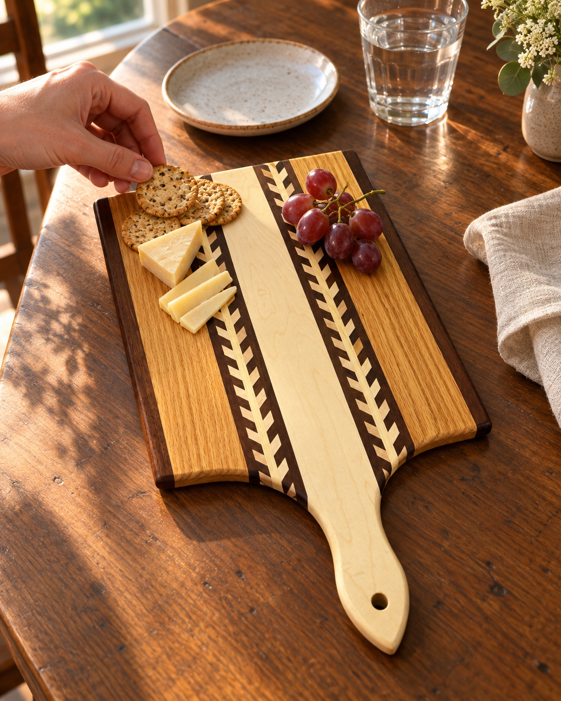 Wheat-pattern paddle board holding a small cheese-and-cracker snack while a hand reaches for a cracker; one board per purchase.