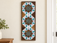 S642 — tall wooden barn quilt banner wall art, three stacked flowers with muted gray-green centers, brown blocks, silver petals and turquoise tips, displayed on an indoor wall in a styled home